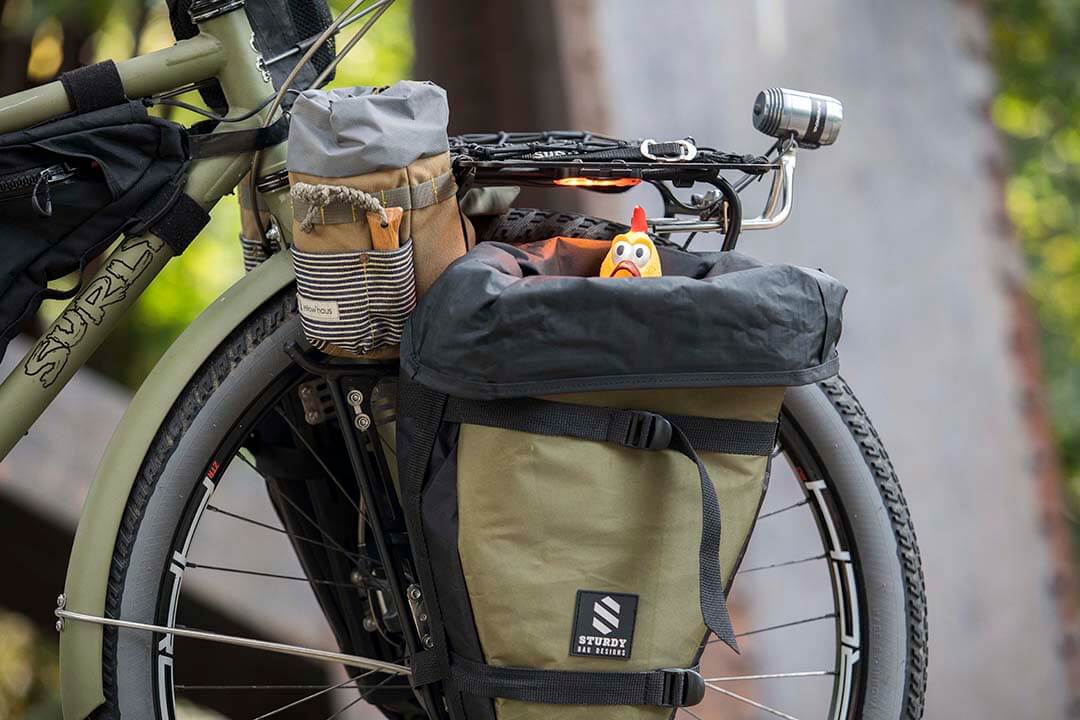 Right side, front end view of an olive drab Surly Bridge Club bike, with a rubber chicken peeking out of fender bag