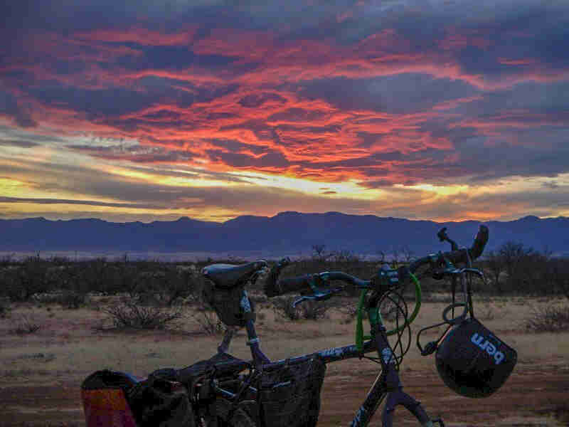 Cropped view of the top of a Surly bike, with a brushy desert and hills in the background and red clouds above