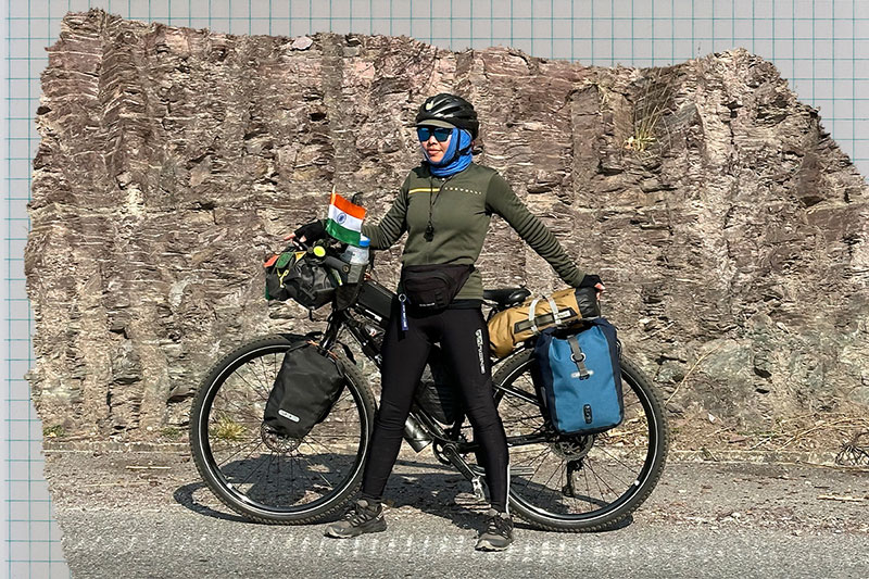 Ashim standing in front of fully loaded touring bike on side of road rock wall in background