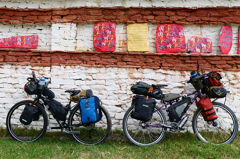Fully loaded touring bikes leaning up agains brikc wall with stone tablets with colorful writing