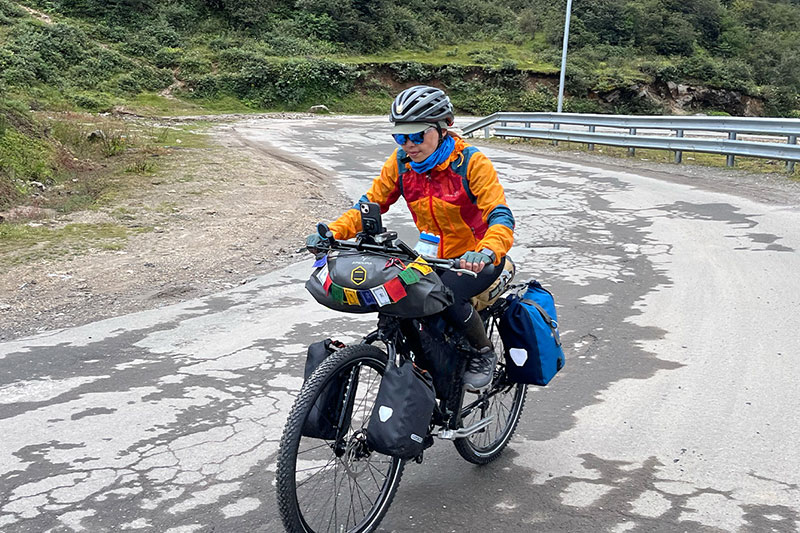 Ashim riding fully loaded touring bike up paved mountain road wearing colorful rain jacket