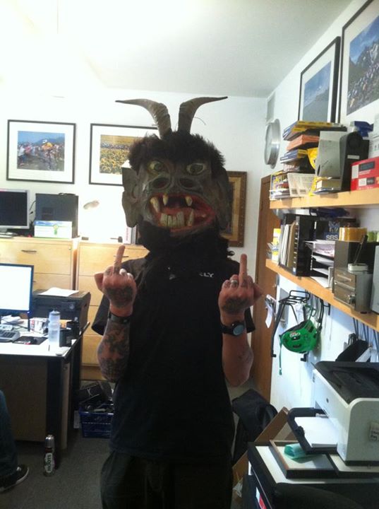 Front view of a person, wearing a krampus costume head, holding up their middle fingers, in an office