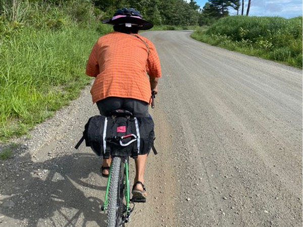 Cyclist riding on gravel road with large seatbag on back