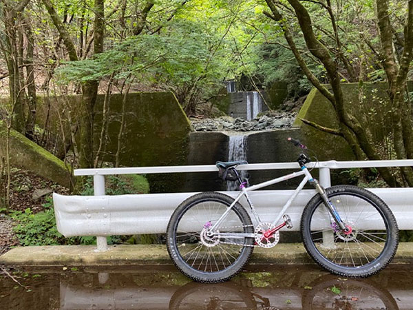 Custom white Surly mountain bike leaning against guard rail in front of small waterfall
