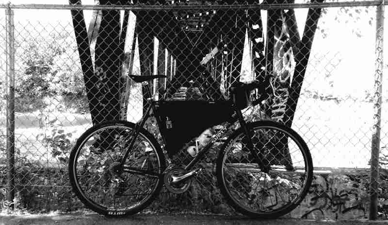 Right profile of a Surly bike, against a chain link fence, with a bridge frame in the background - black & white image