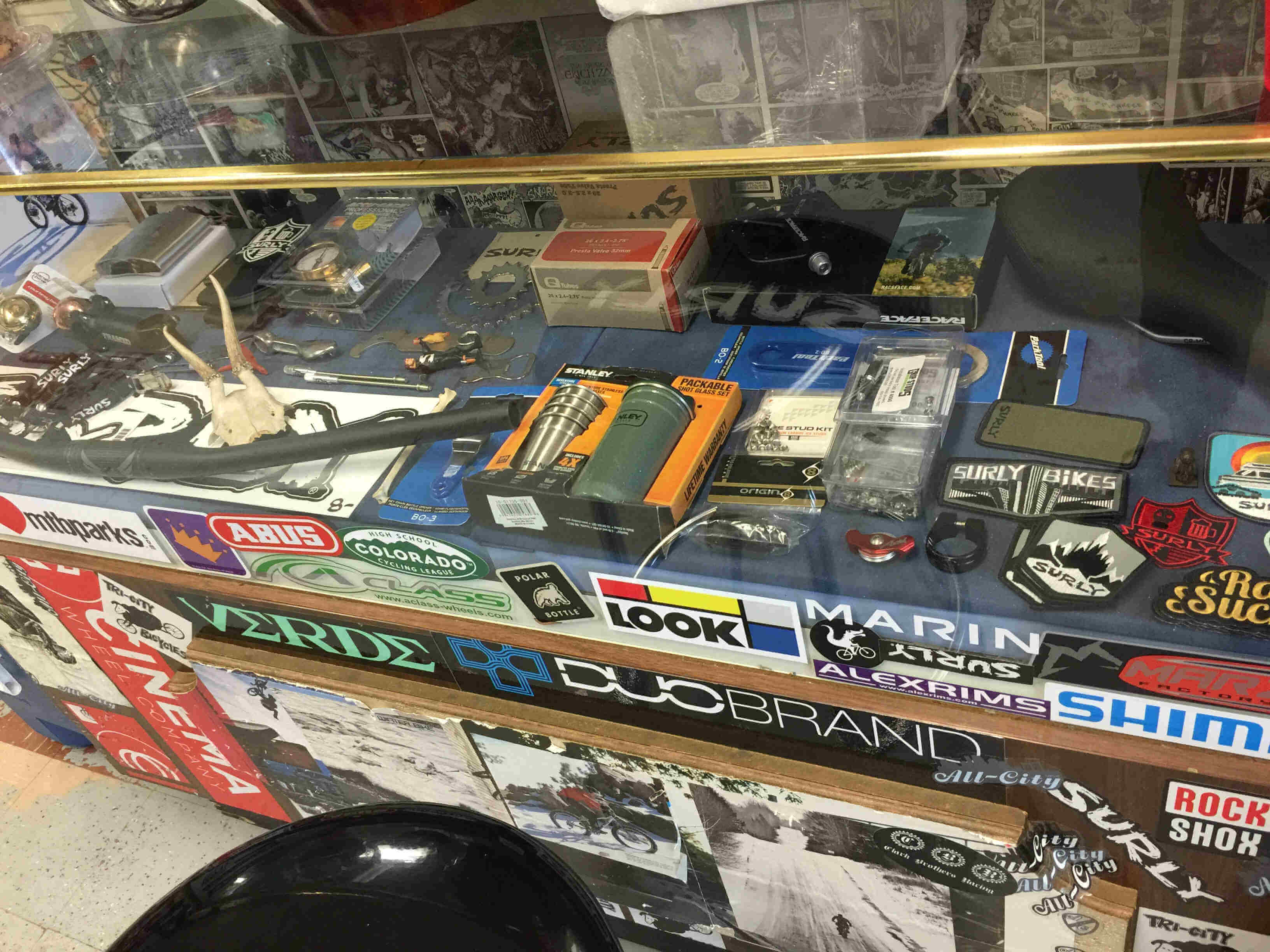 Downward view of a counter covered in various stickers, bike parts inside the glass case
