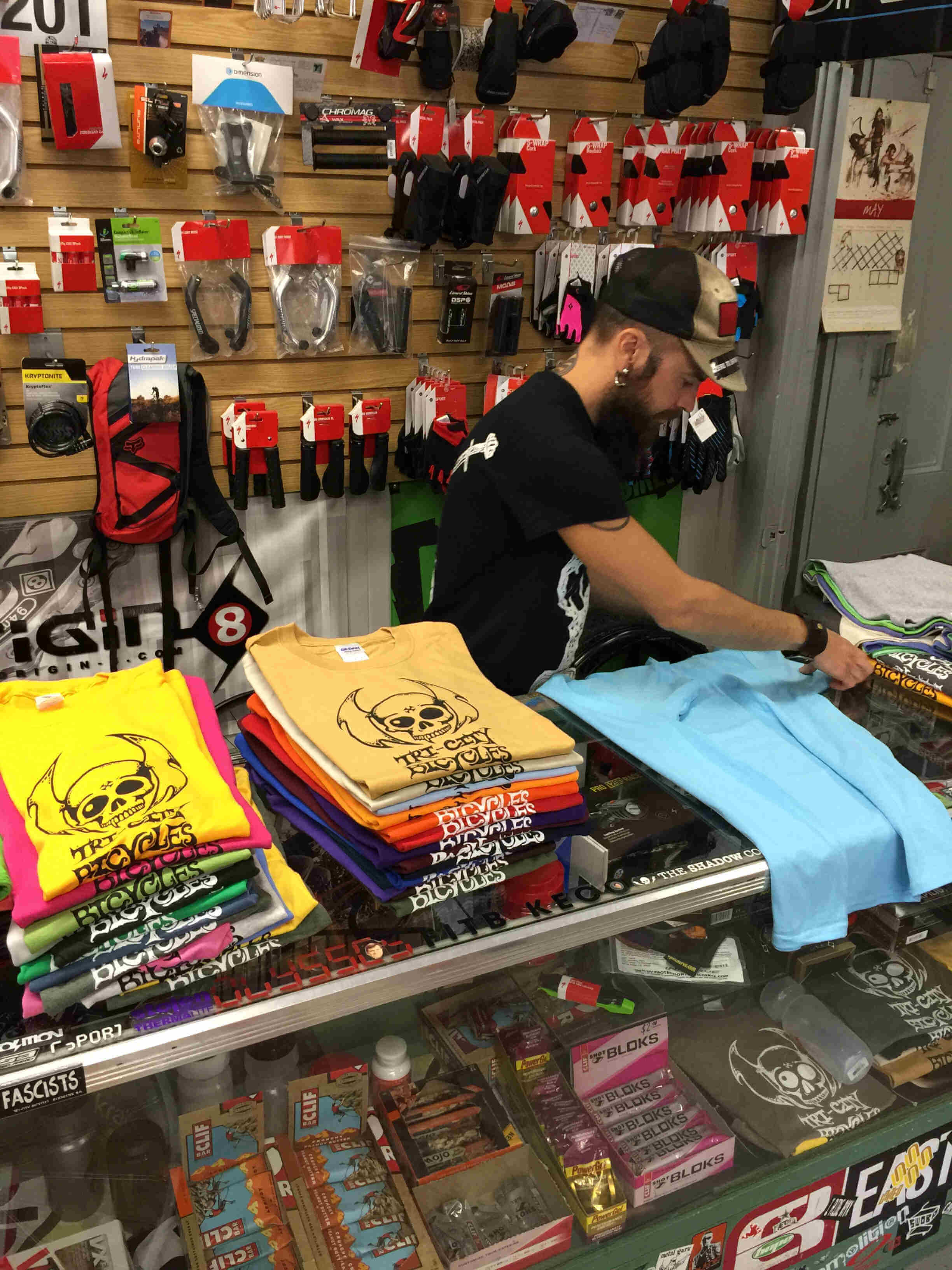 A person behind a service counter, folding t-shirts, with a wall of packaged bike parts behind them