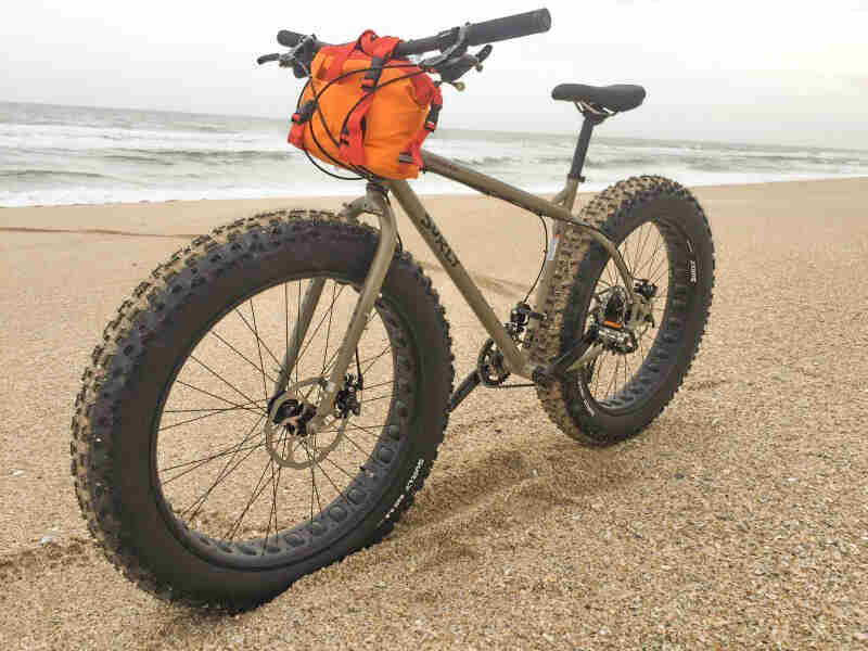Left side view of a tan Surly fat bike, parked on a beach with the ocean in the background