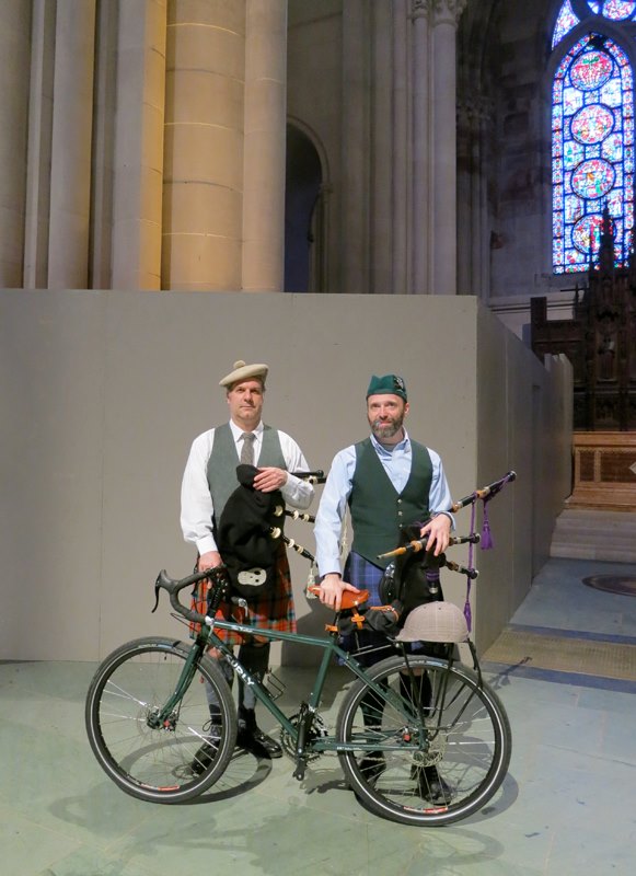 Left side view of a green Surly Disc Trucker bike, with 2 men in kilts, standing on the right side inside a cathedral