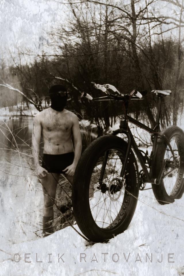 Front, left side view of a Surly fat bike, on a snowy pond bank, with a person behind, standing in water - black & white