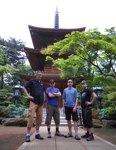Front view of 4 people, standing side by side on a stone block walkway, with a Japanese shrine behind them