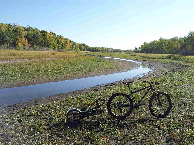 Right side of a green Surly Krampus bike and trailer, parked on a grassy part of a river bottom valley