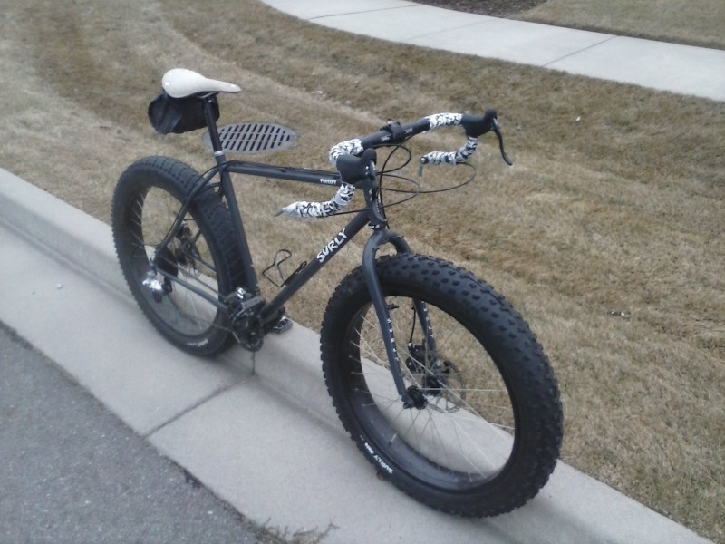 Front, right side view of a black Surly Pugsley fat bike, leaning against a street curb