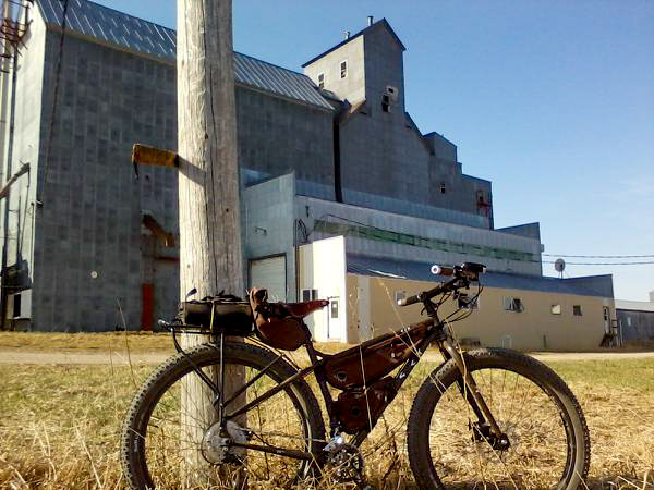 Right side view of a Surly bike, parked on grass in front of a telephone pole, with a grain building in the background