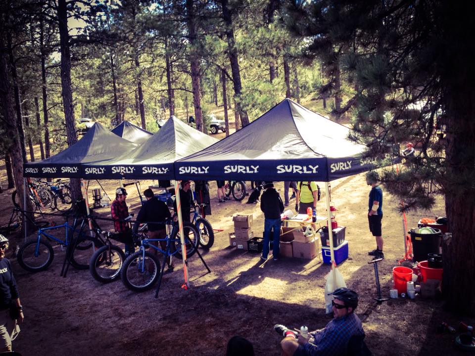 A 3 section Surly canopy, with people, bikes and gear underneath, in the forest