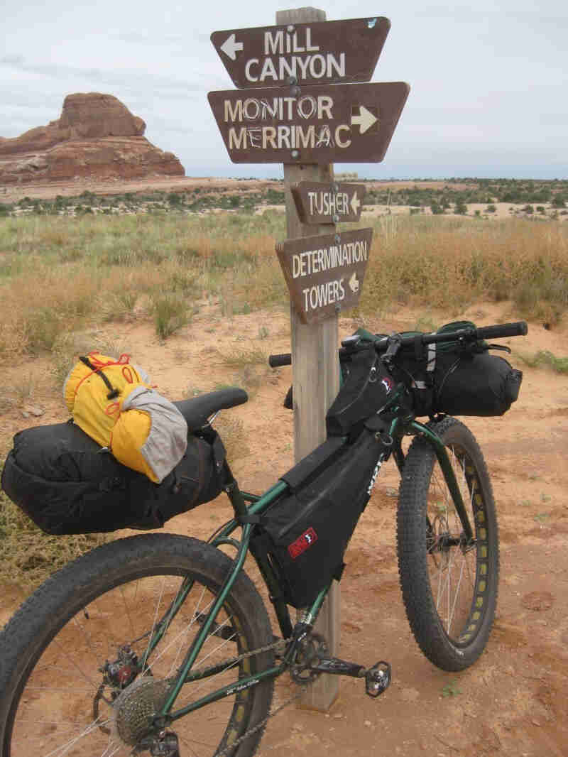 Right side view of a green Surly Krampus bike, leaning against a wood post with direction signs, on desert field