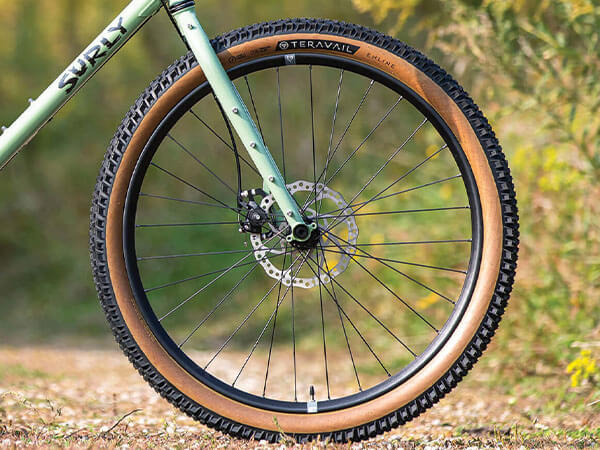 View of front wheel/tire and Dinner Fork on Grappler complete bike, outside on gravel road