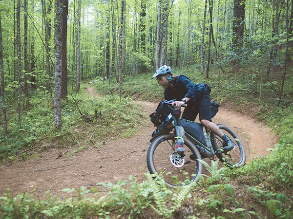 Person riding Grappler loaded for bikepacking on forest singletrack, going around banked corner