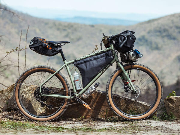 Surly Ghost Grappler loaded for bikepacking: frame pack, seatpack, handlebar bag, small front rack, mountains in background