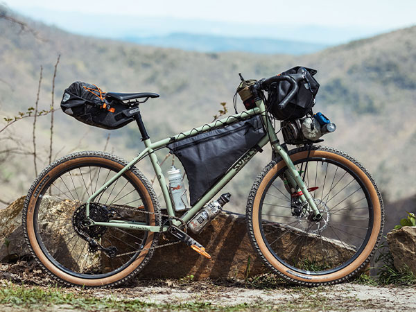 Surly Grappler loaded for bikepacking: frame pack, seatpack, handlebar bag, small front rack, mountains in background