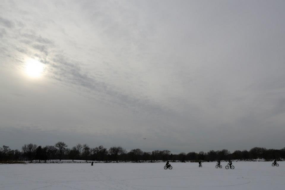 A handful of cyclists riding around on a frozen lake with bare trees around it