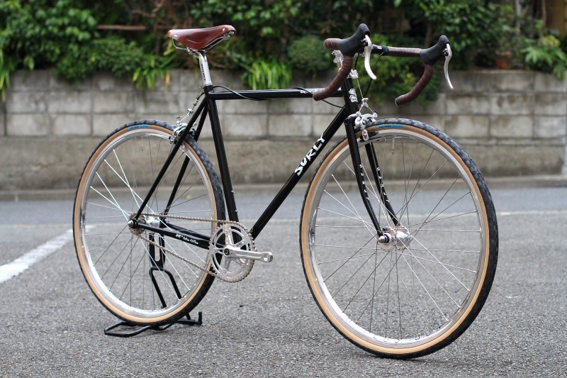 Right side view of a black Surly bike, standing on a paved parking lot, with a cement block wall in the background