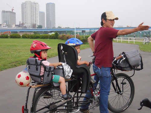Rear, right side view of a Surly Big Dummy bike, with a cyclist in front and 2 children in back, facing a city skyline