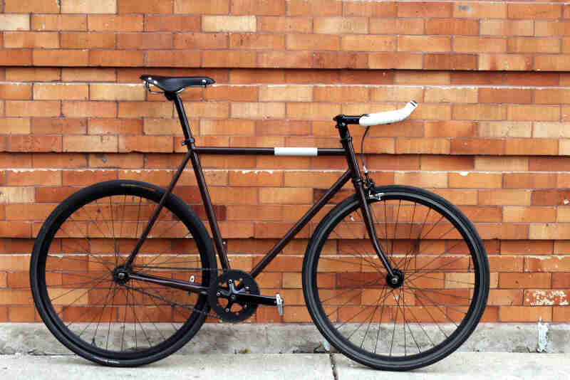 Right profile of a black Surly bike, on a sidewalk, against an orange brick wall