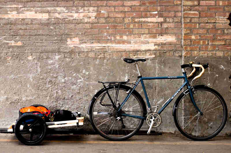 Right profile of a Surly Long Trucker bike, with a bike trailer loaded with gear connected, parked along a brick wall