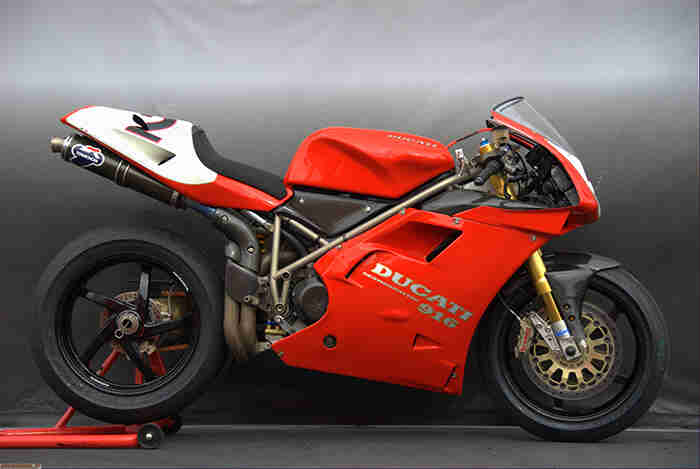 Right profile of a red Ducati 916 sport motorcycle with a gray background behind