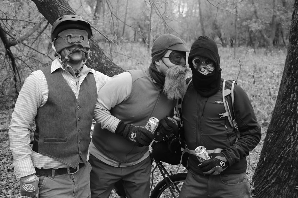 Front view of 3 people wearing masks, standing in the woods, black & white image