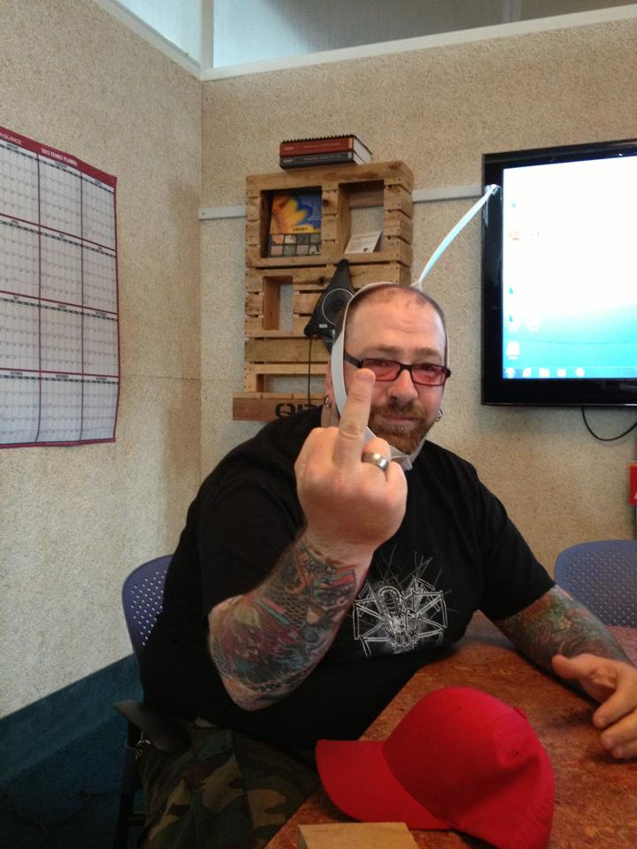 Front view of a person, with a strap around their head, showing their middle finger, and sitting at an office table