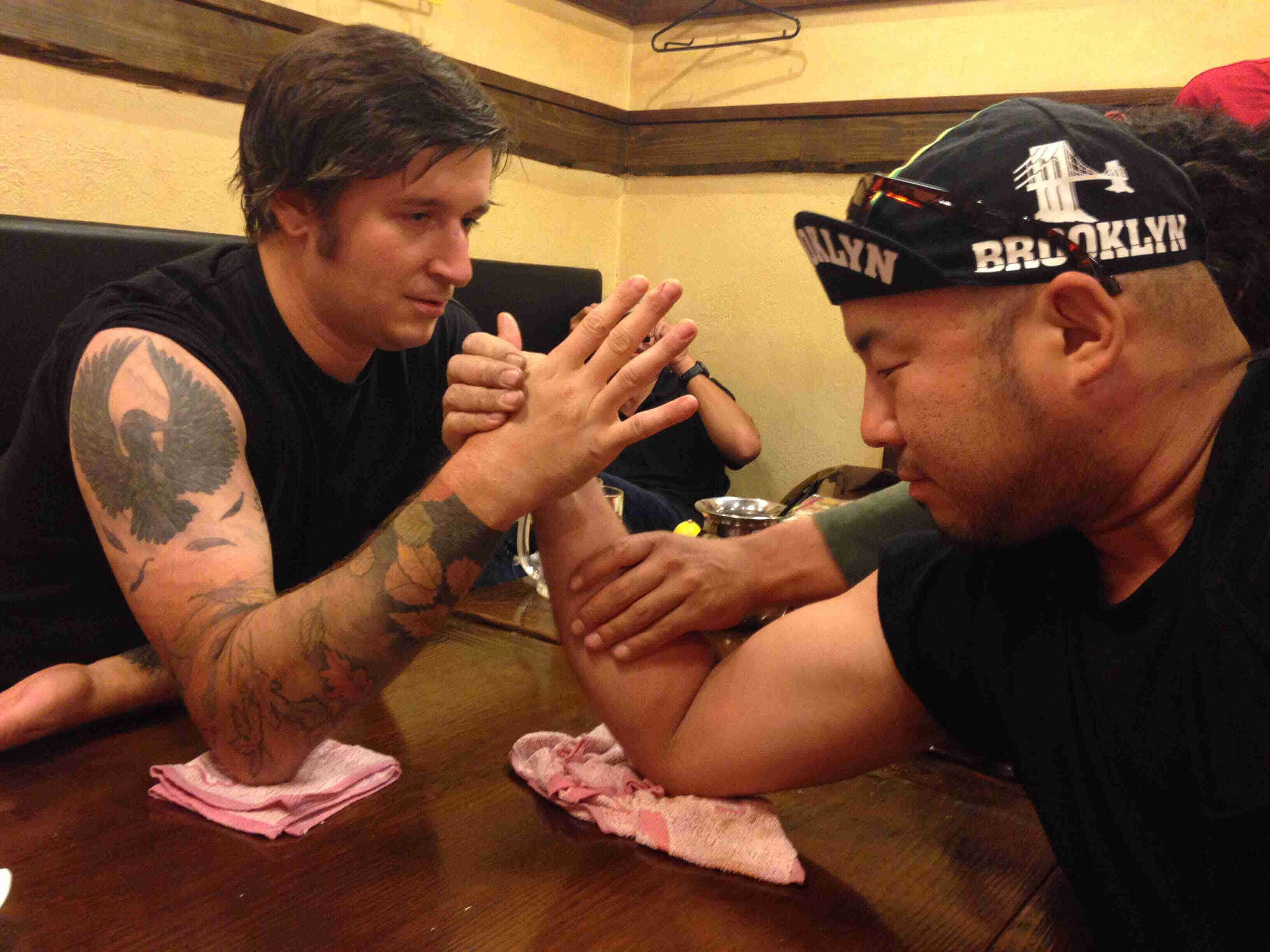 Side view of two people sitting across from each other, arm wrestling at a table