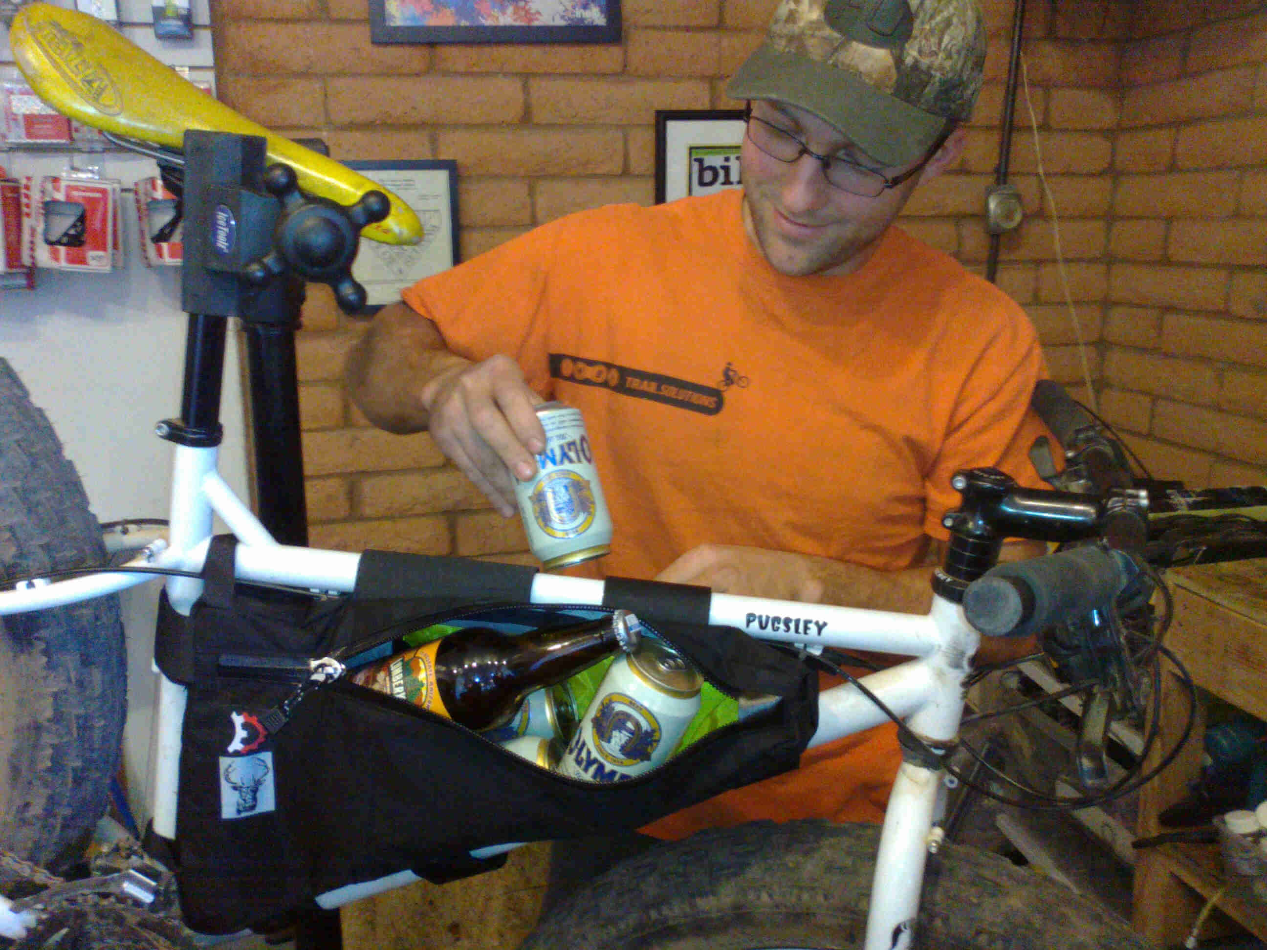 Right side view of a white Surly Pugsley fat bike, in a bike shop, with a person stuffing beer cans in the frame bag