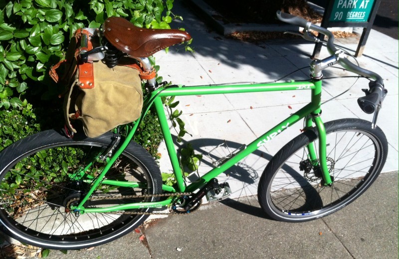 Right side view of a green Surly 1x1 bike, against a hedge bush, on a sidewalk
