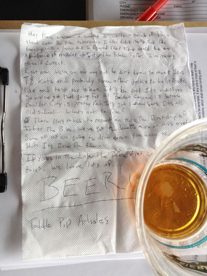 Downward view of a letter, written on a white napkin, with a plastic glass of beer set on the bottom