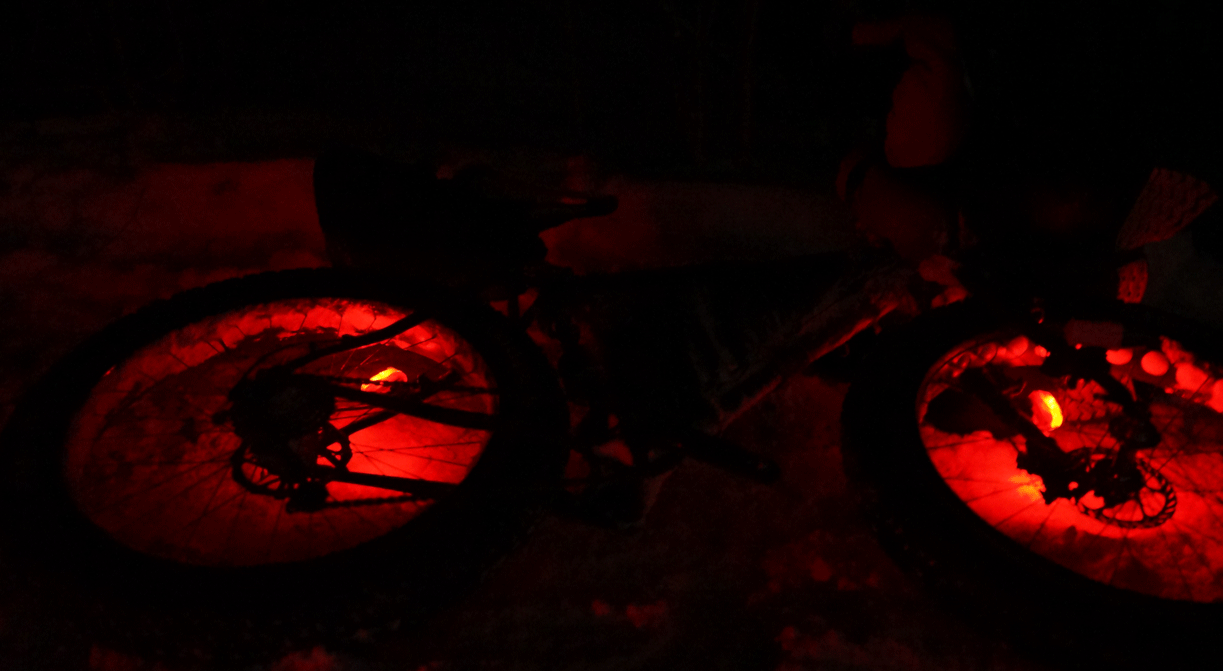 Looped GIF of a red flashing lights in the wheel spokes of a fat bike laying in the snow at night