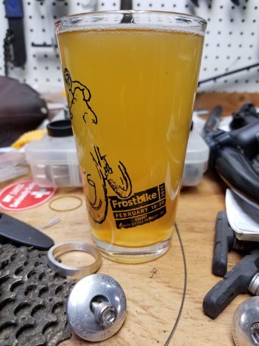 Full glass of beer sitting on workbench and pegboard with various small bike part surrounding the glass