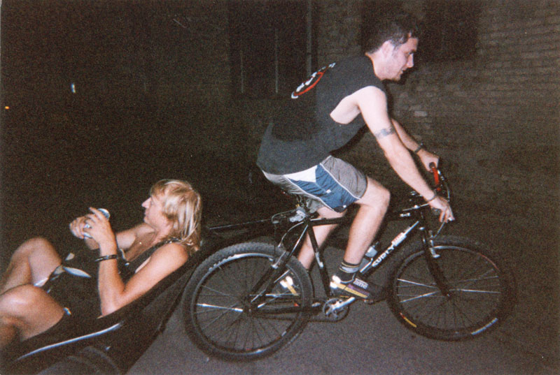 Right side view of a cyclist, riding a Surly bike with a person in a trailer attached, in the dark at night