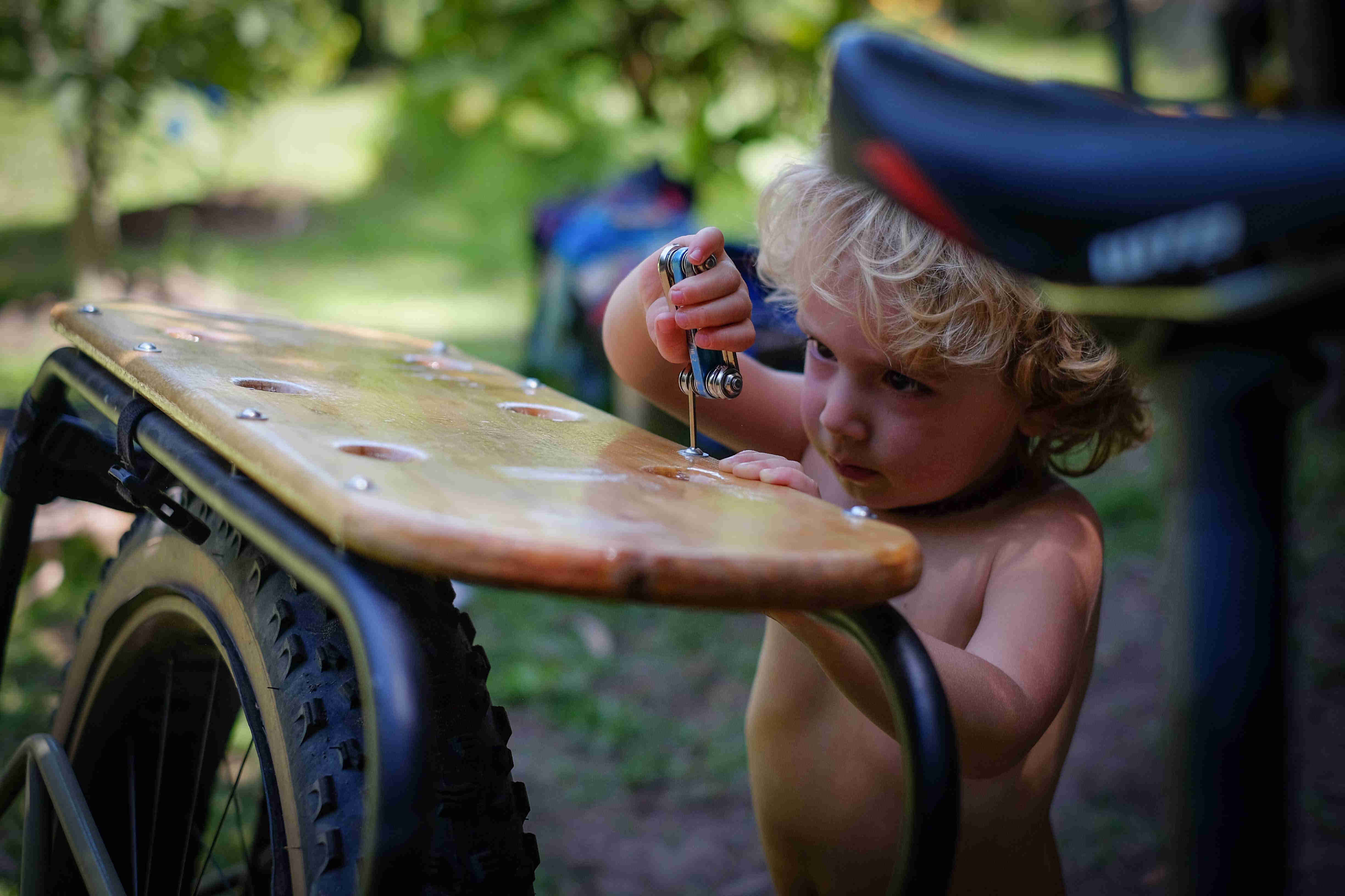 Close up of a small child tightening a screw on the rear wood rack of a Surly Big Fat Dummy bike