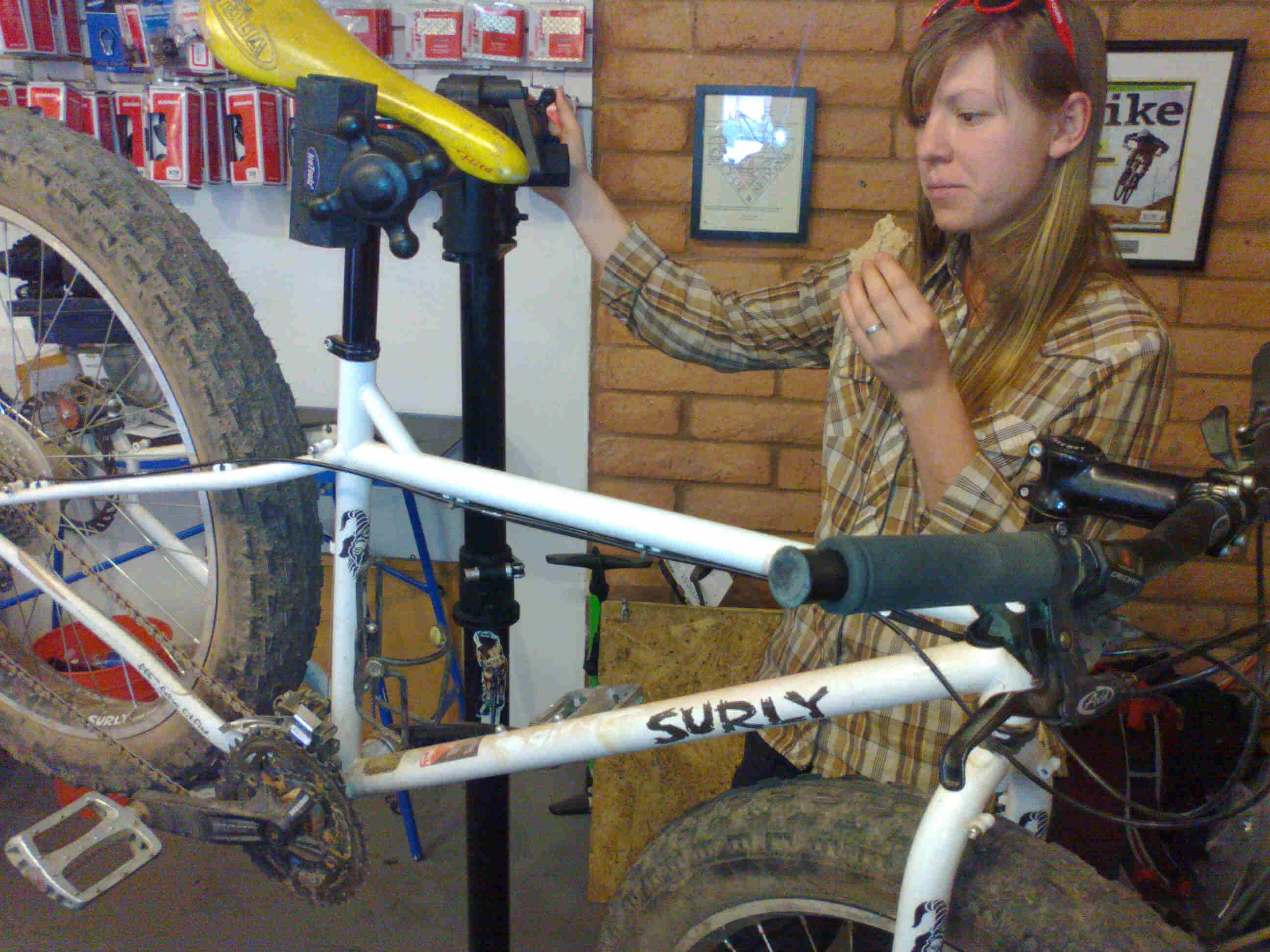 Right side view of a white Surly Pugsley fat bike, on a repair stand in a bike shop, with a person standing behind it