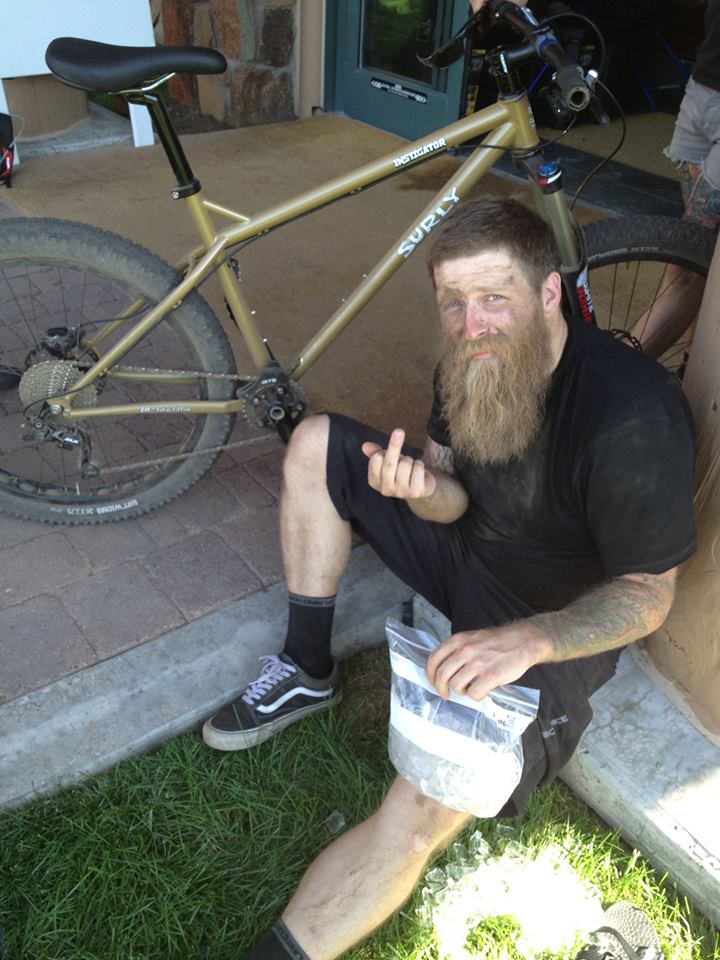 Downward view of a person, sitting in front of a Surly Instigator bike, icing their knee and showing their middle finger