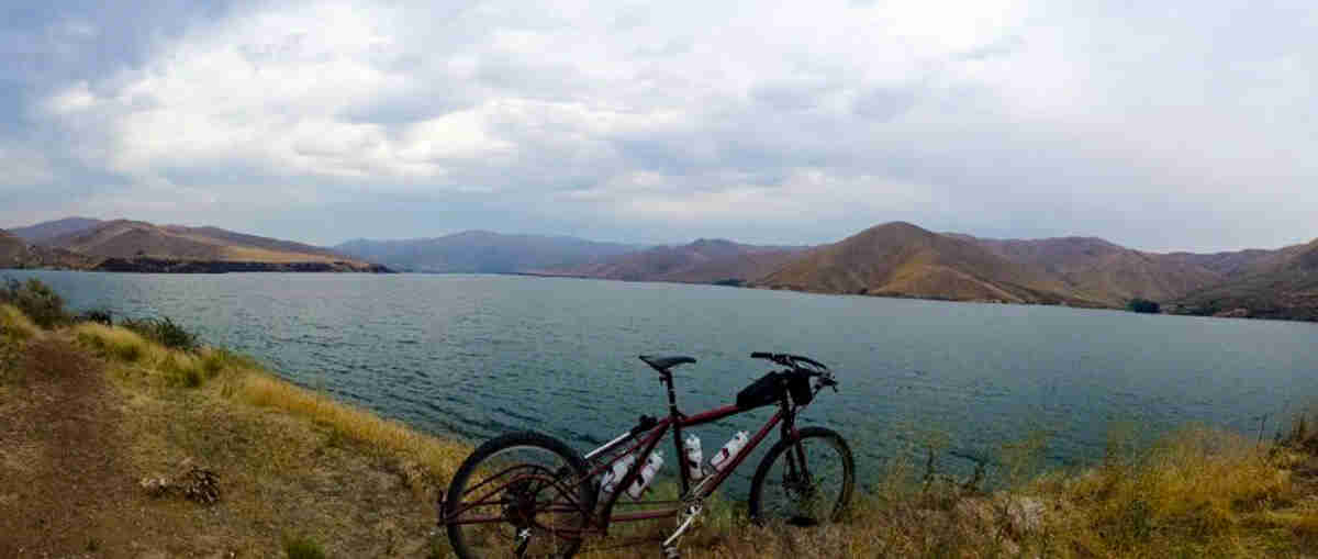 Right side view of a red Surly Big Dummy bike, parked on the edge of a lake, with mountains in the background