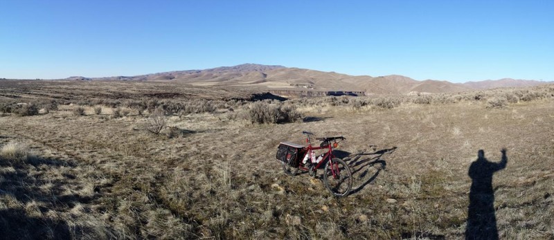 Panoramic, front, right side view of a red Surly Big Dummy bike, parked in a grassy plains field