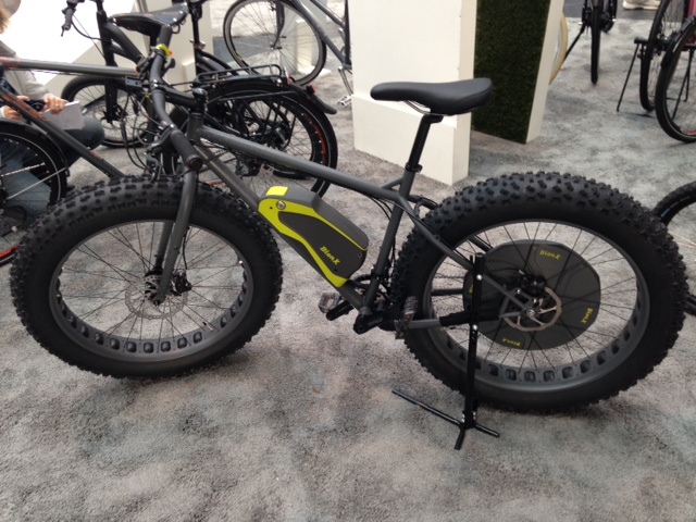 Left side view of a gray Surly Moonlander BionX electric fat bike, standing on gray carpet with other bikes around it