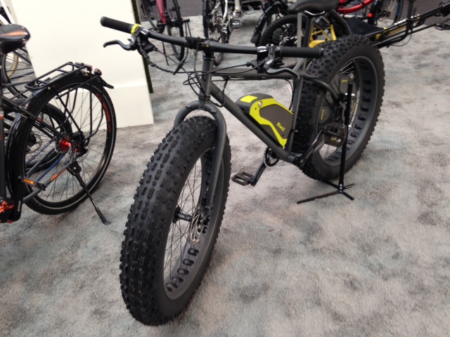 Front, left side view of a Surly Moonlander BionX electric fat bike, standing on gray carpet with other bikes around it