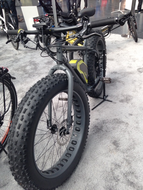 Front, left side view of a Surly Moonlander BionX electric fat bike, parked on gray carpet with other bikes around it
