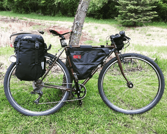 Right profile of a Surly Cross Check bike, loaded with gear, parked in a grass field, with trees in the background