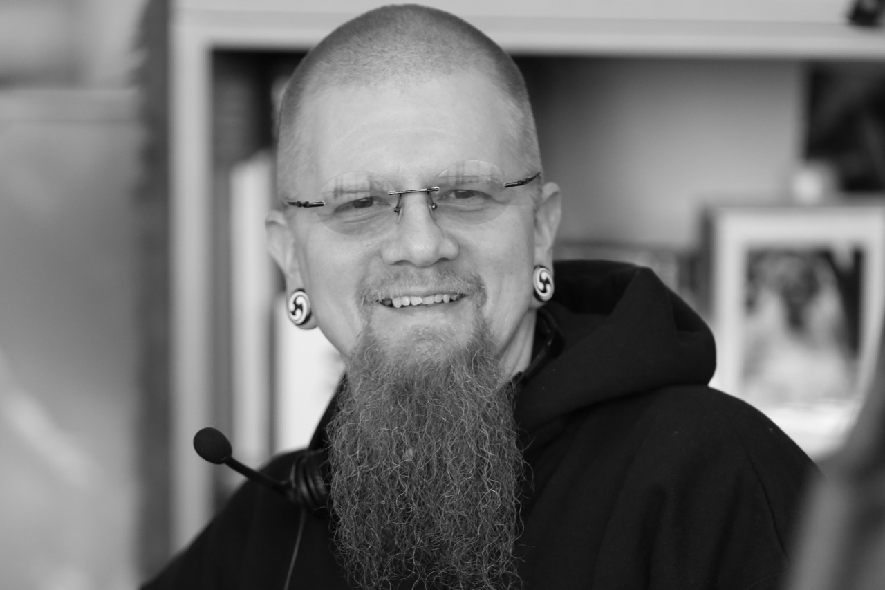 Headshot of a person with a long, narrow beard and wearing glasses - black & white image