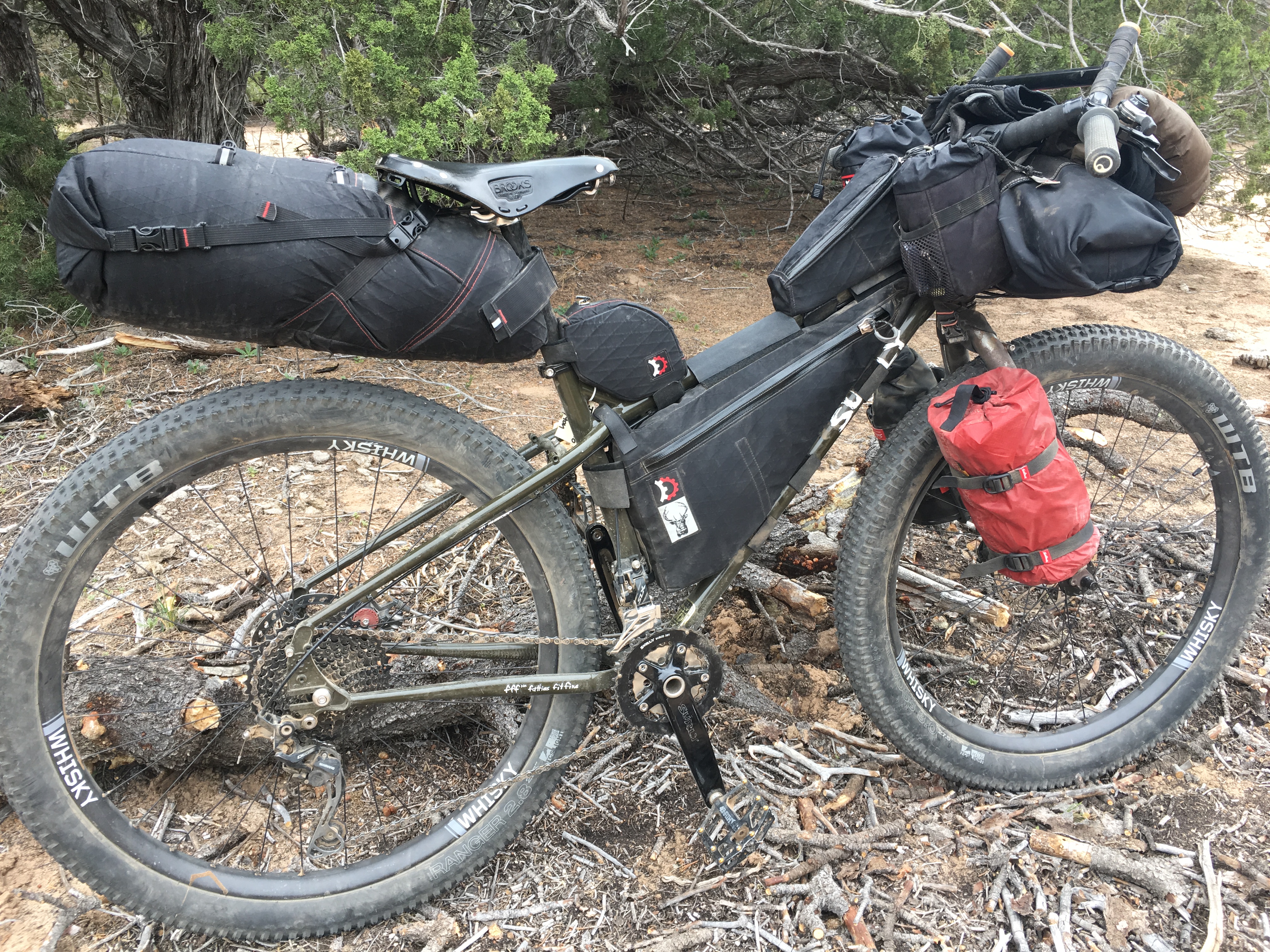 Right side view of a Surly bike, black, loaded with gear, standing in sticks and dirt with brushy trees in background